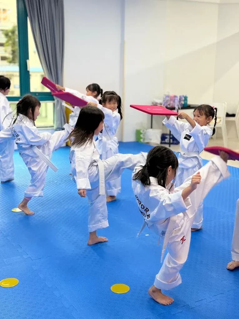 Students mid-kick, striking pads held up by their classmates.